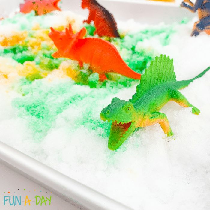 Closeup of a green dinosaur toy in painted snow tray.