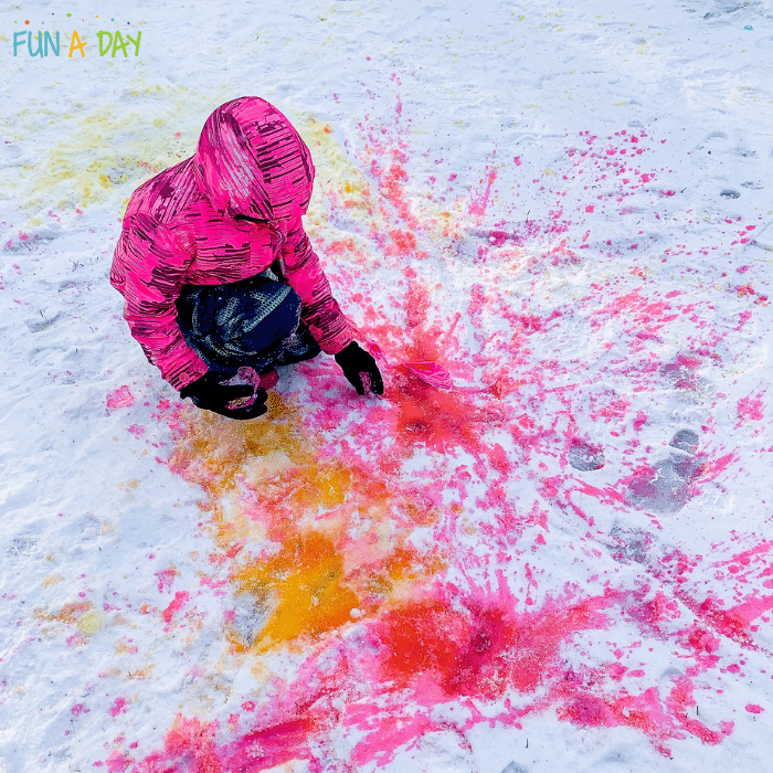 Child inspecting pink and orange snow splat painting