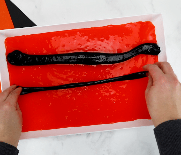 Person stretching out strips of black slime on a bed of orange slime, creating the tiger stripes.