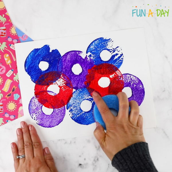 Using a cut up pool noodle piece to stamp blue, red, and purple paint