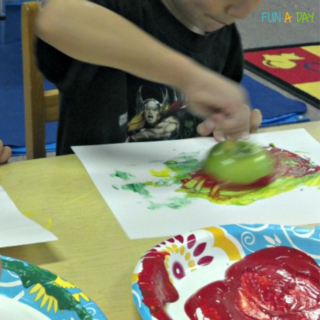 child vigorously painting with apple and tempera paint