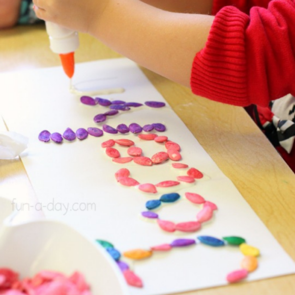 preschooler gluing dyed pumpkin seeds to write her name
