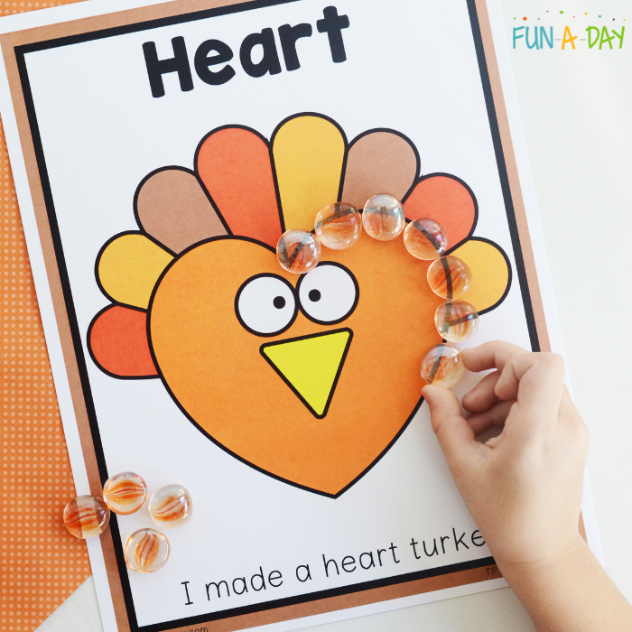 preschool hand adding glass gems to a heart-shaped turkey mat