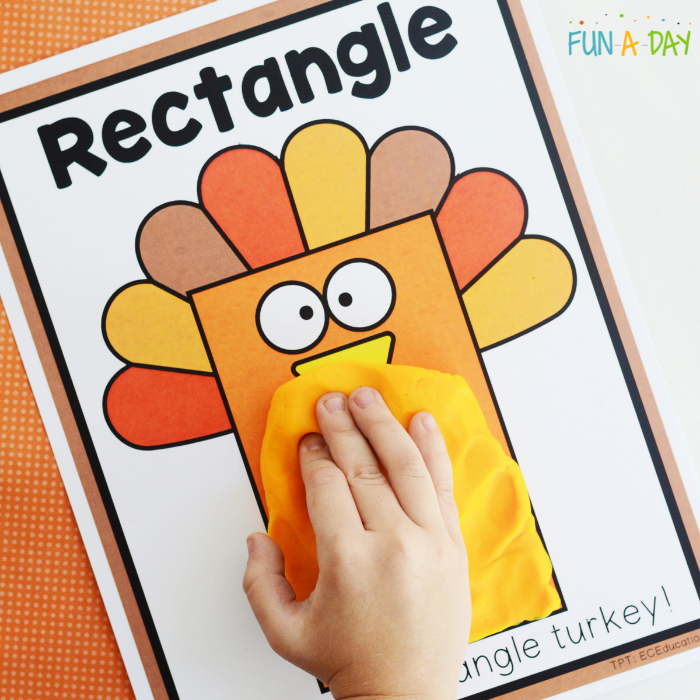 preschool hand adding orange play dough to turkey shape mat
