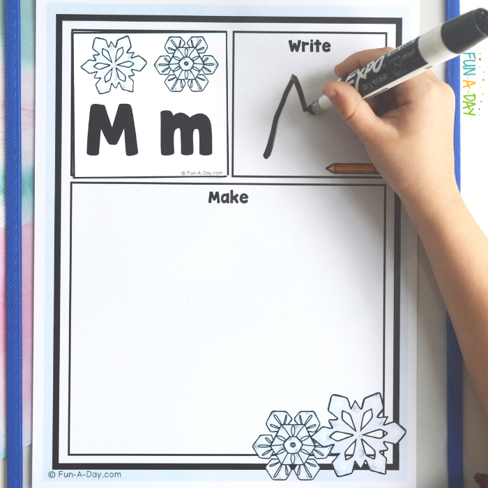 preschooler's hand using a dry erase marker to write M on winter read it write it build it printable