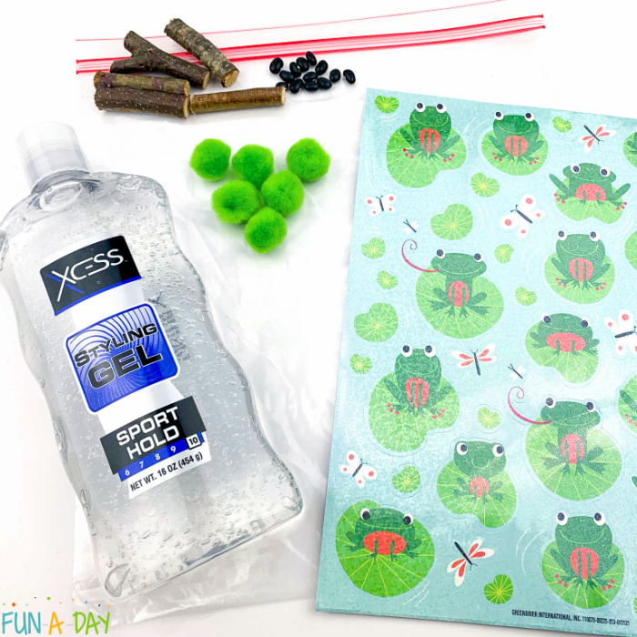 supplies for diy frog sensory bag: clear hair gel, plastic gallon bag, sticks, pom poms, and black beans