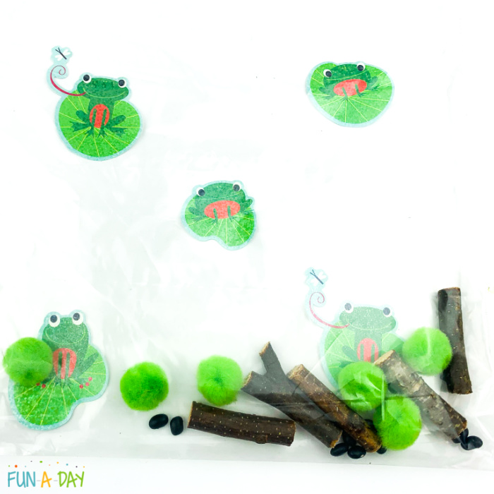 supplies for preschool frog sensory bag - frog stickers, sticks, pom poms, and beans inside of bag