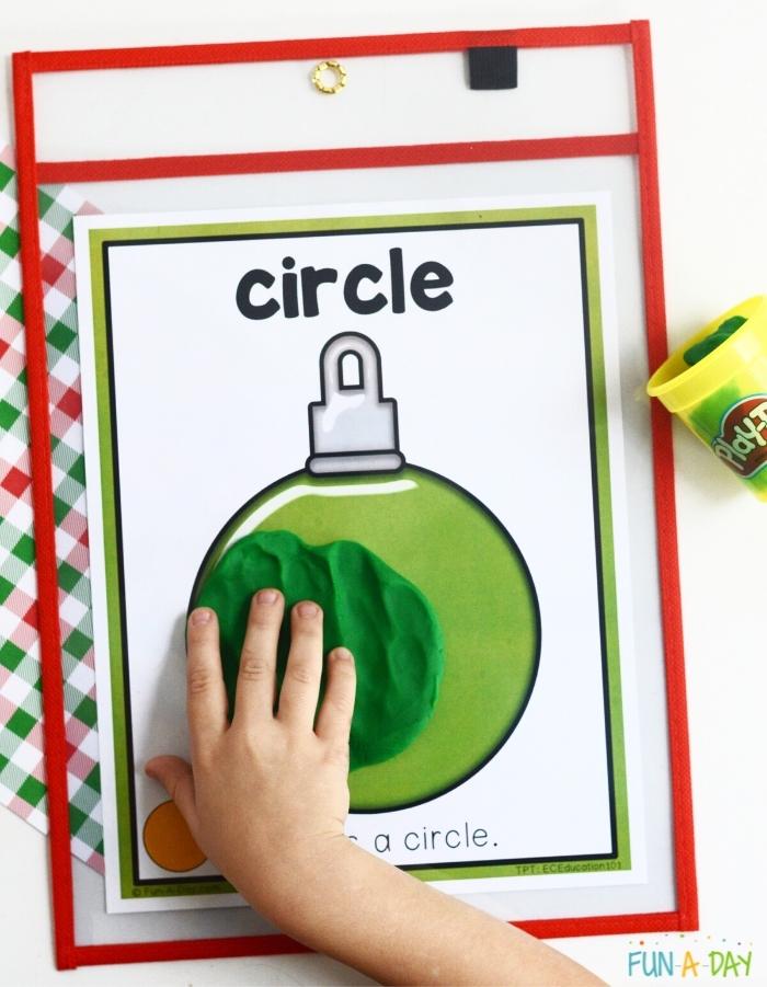 child's hand pressing green playdough onto a circle ornament printable to match the shape