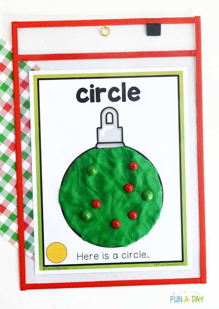 photo of circle ornament shape inside of dry erase pocket with green playdough in the shape of the ornament; red and green manipulatives pressed into playdough
