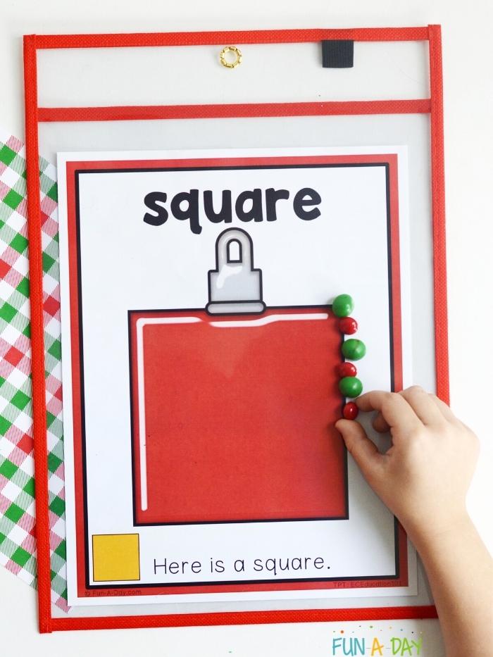 preschool worksheet printable inside of dry erase pocket - child's hand placing red and green items on outside line of square christmas ornament to trace the shape