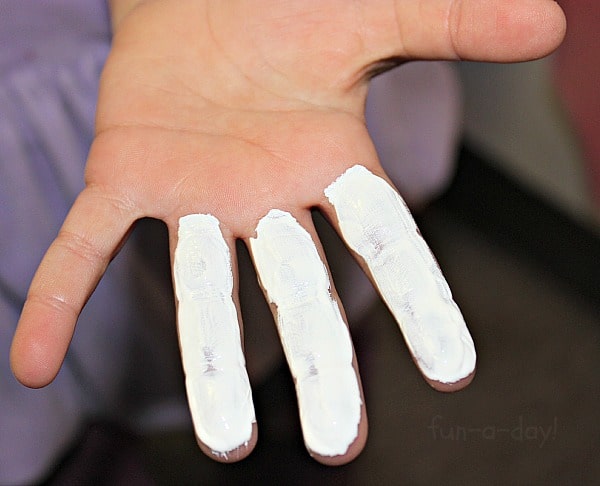 Child's hand with white paint on 3 fingers from making a snowman ornament keepsake