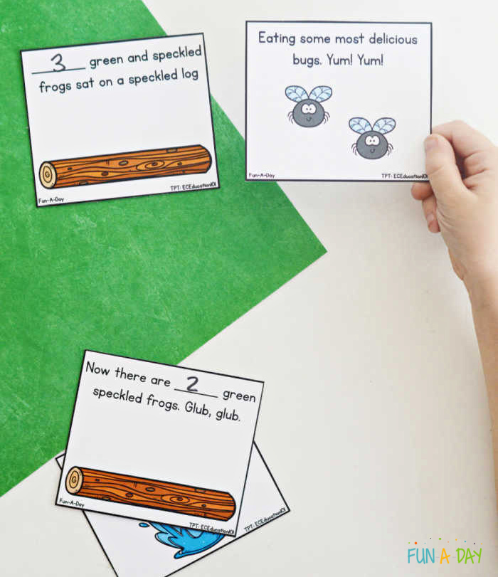 child's hand holding up a sequence card printable from 5 green and speckled frogs math activity