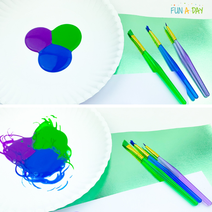 Purple, green, and blue paint poured so that they're touching on a plate with paintbrushes to the side. 