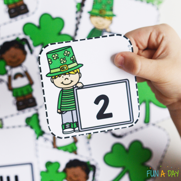 child's hand holding up a st. patrick's day calendar number card for preschool math practice