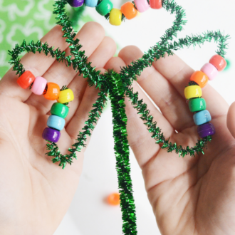 Child holding a shamrock craft made with pipe cleaner and pony beads