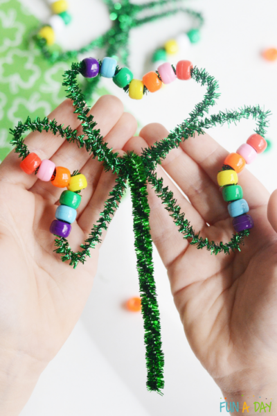 Child holding a shamrock craft made with pipe cleaner and pony beads
