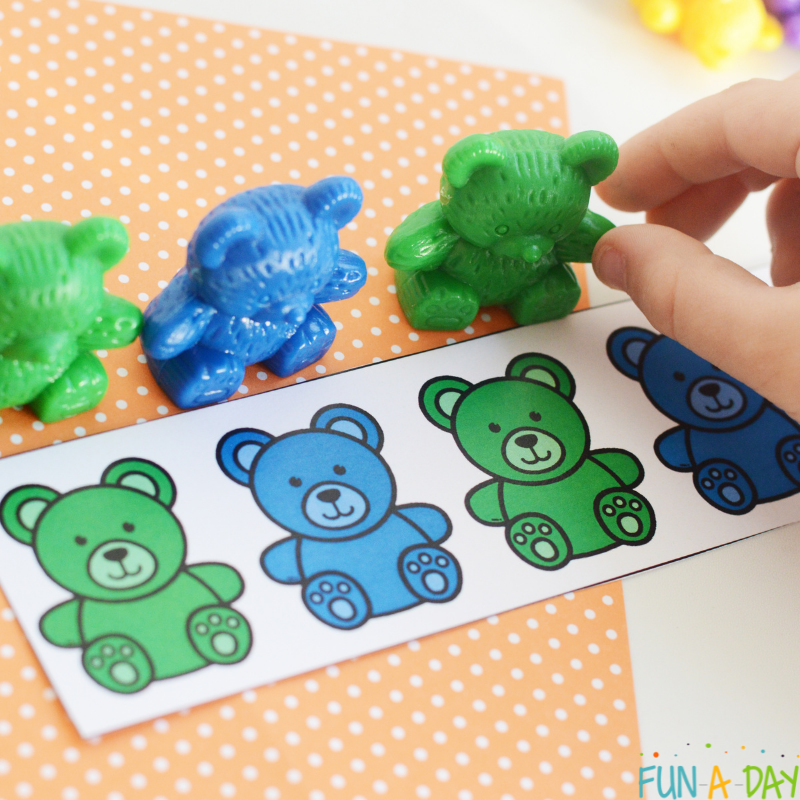 Close up of child's hand placing green and blue counting bears on free printable pattern cards