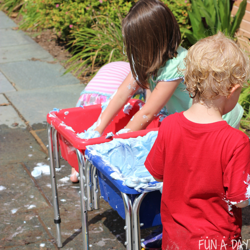 preschoolers playing outside in a sensory bin of colored shaving cream