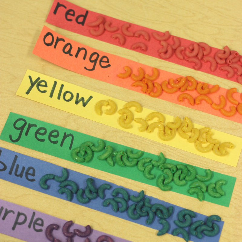 Rainbow macaroni sorted onto colorful strips of paper with color words written on them.