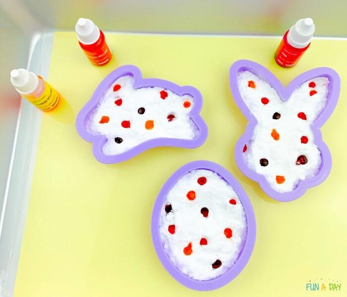 baking soda and food coloring inside of Easter cookie cutters on a tray