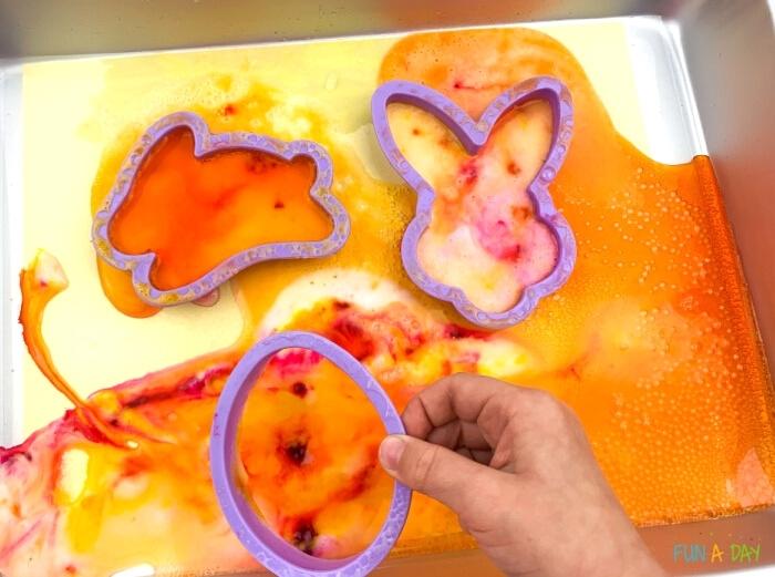 child's hand holding up Easter cookie cutter that has been used in fizzy science experiment