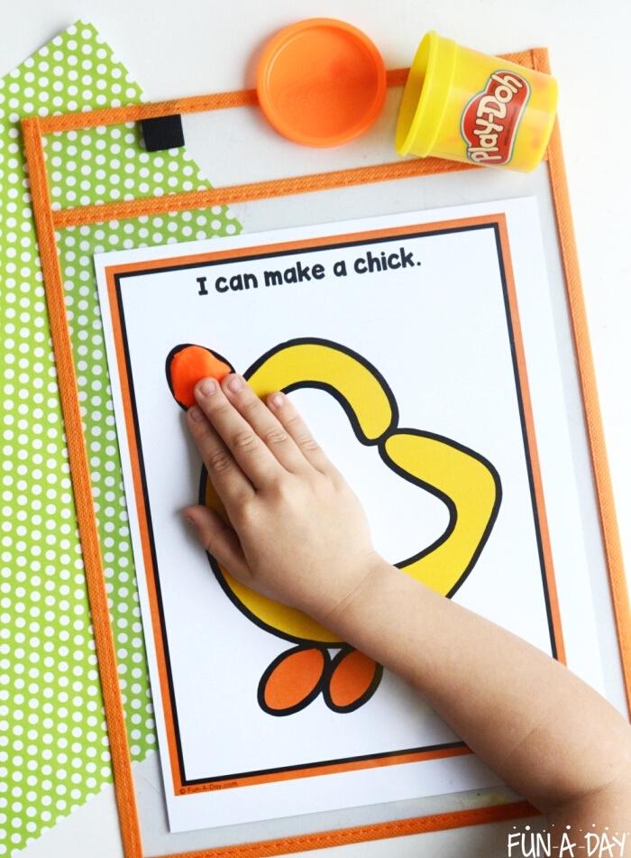child's hand pressing play dough onto a chick Easter play dough mat
