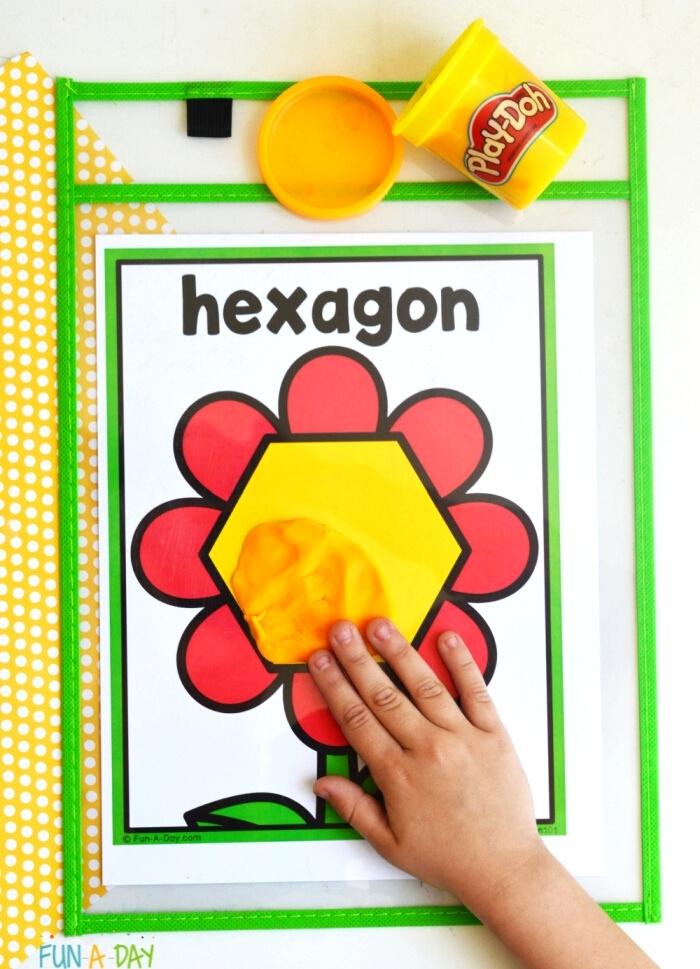 child's hand spreading play dough on a hexagon flower shape mat