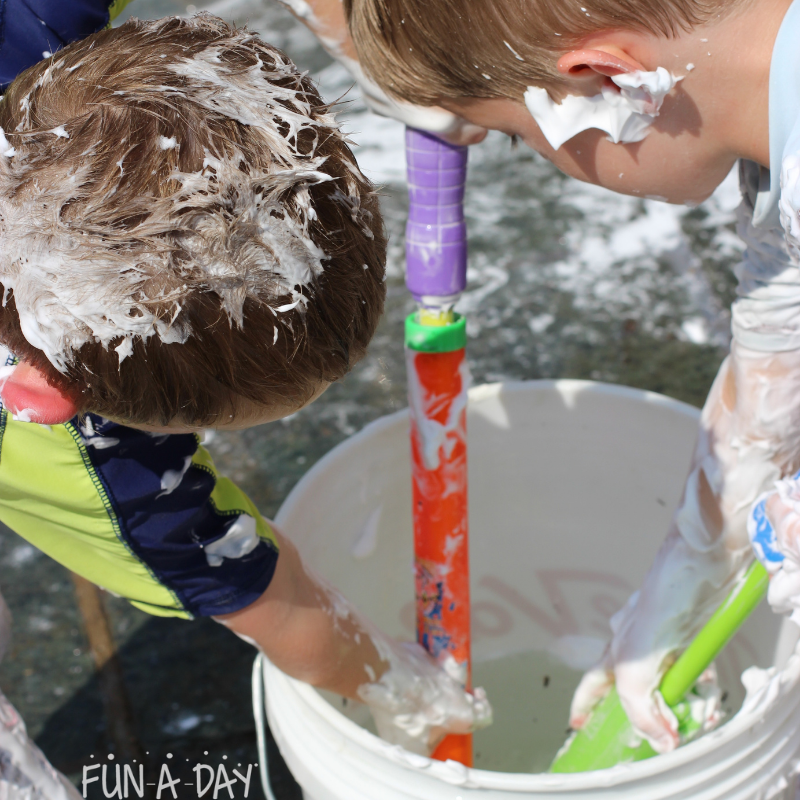 2 preschoolers covered in shaving cream putting water squirters into a bucket