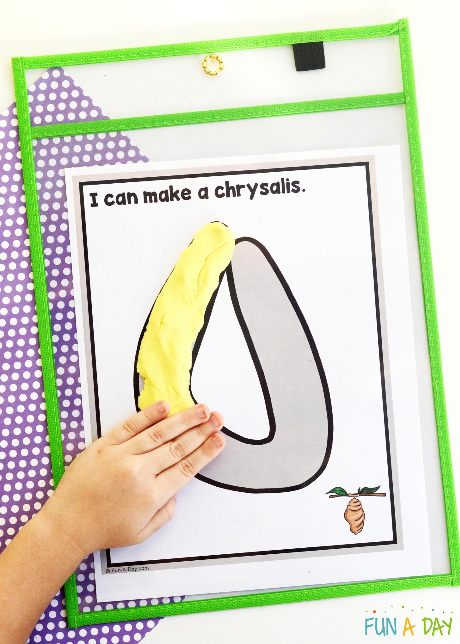 child's hand pressing play dough onto mat showing a butterfly chrysalis