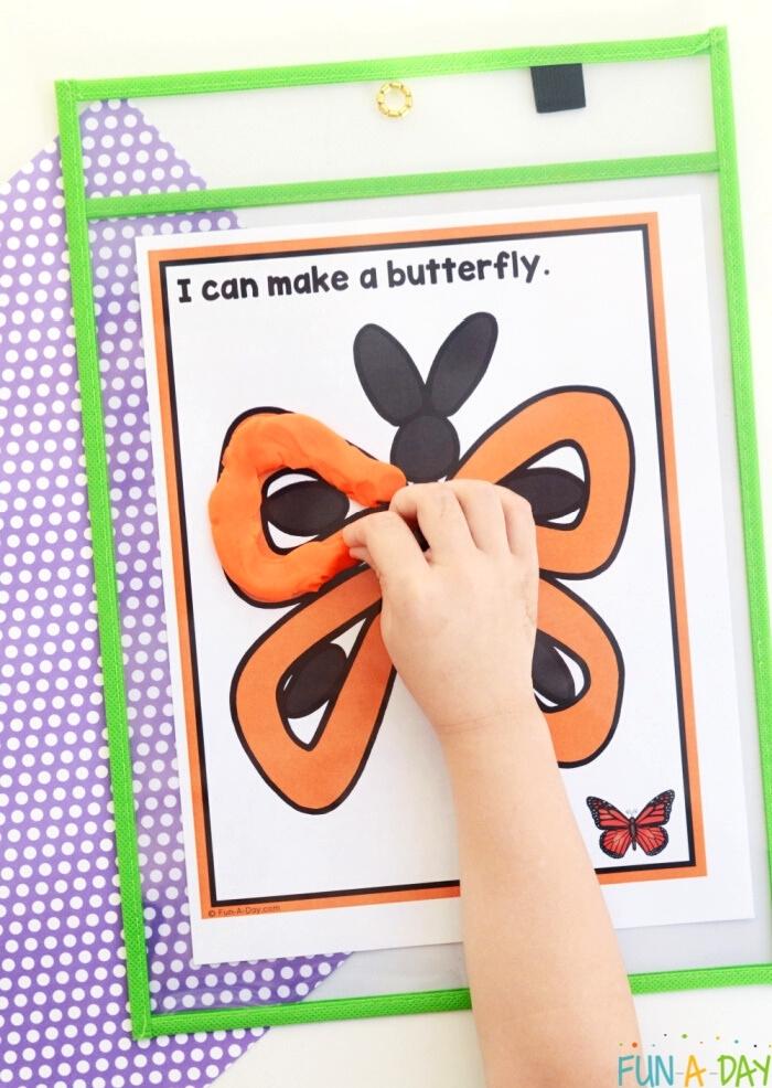 child's hand forming play dough butterfly wings onto a printable