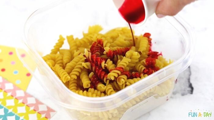 hand pouring red dye into a container of dried pasta