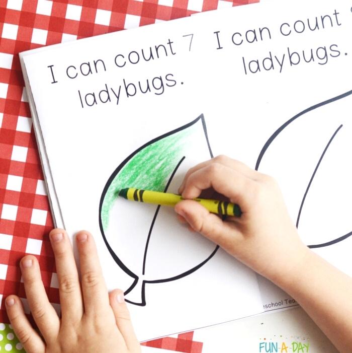 child's hand coloring printable book with a green crayon. Page reads I can count 7 ladybugs