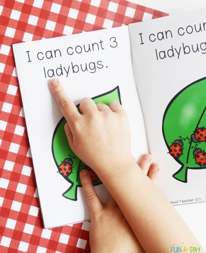child's hand pointing at words in printable book. Page reads: I can count 3 ladybugs