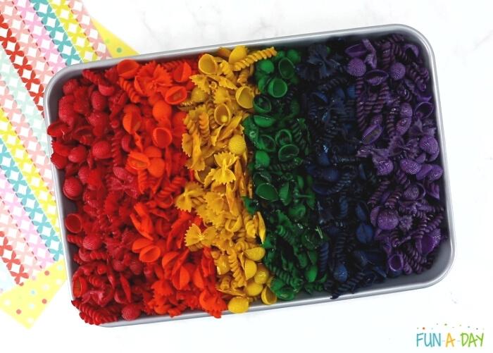 large tray full of dyed pasta sorted into rainbow colors to use in a butterfly sensory bin for kids