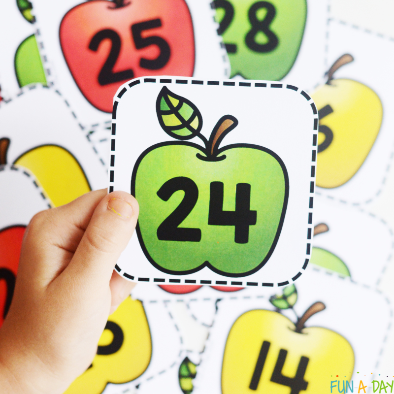 preschooler's hand holding number 24 over apple calendar numbers