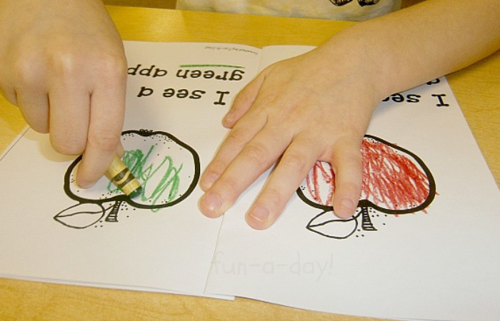 child using green crayon to color an apple mini book