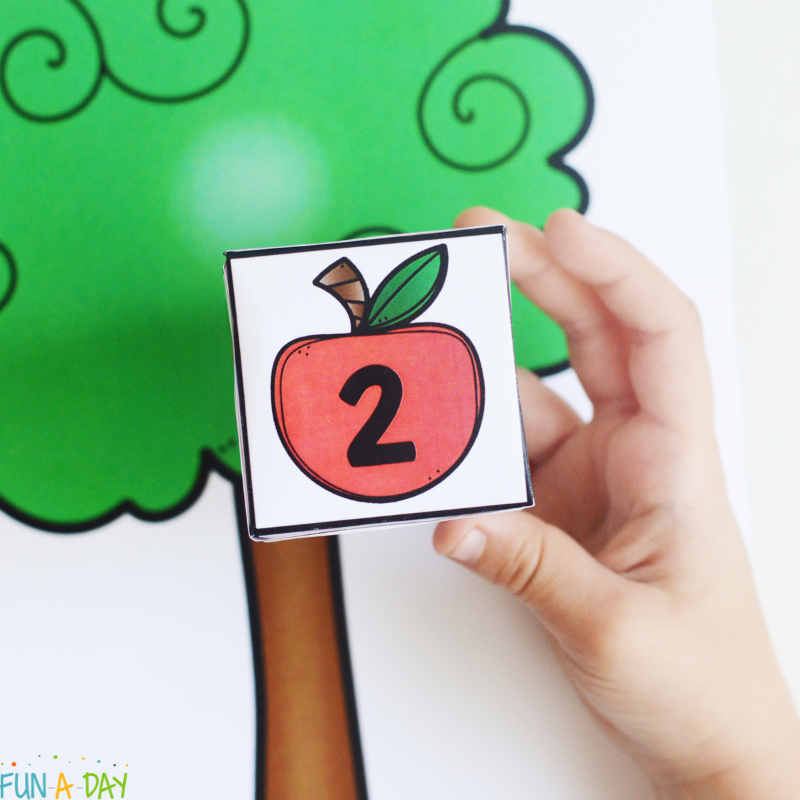 Preschooler's hand holding up apple-themed number cube