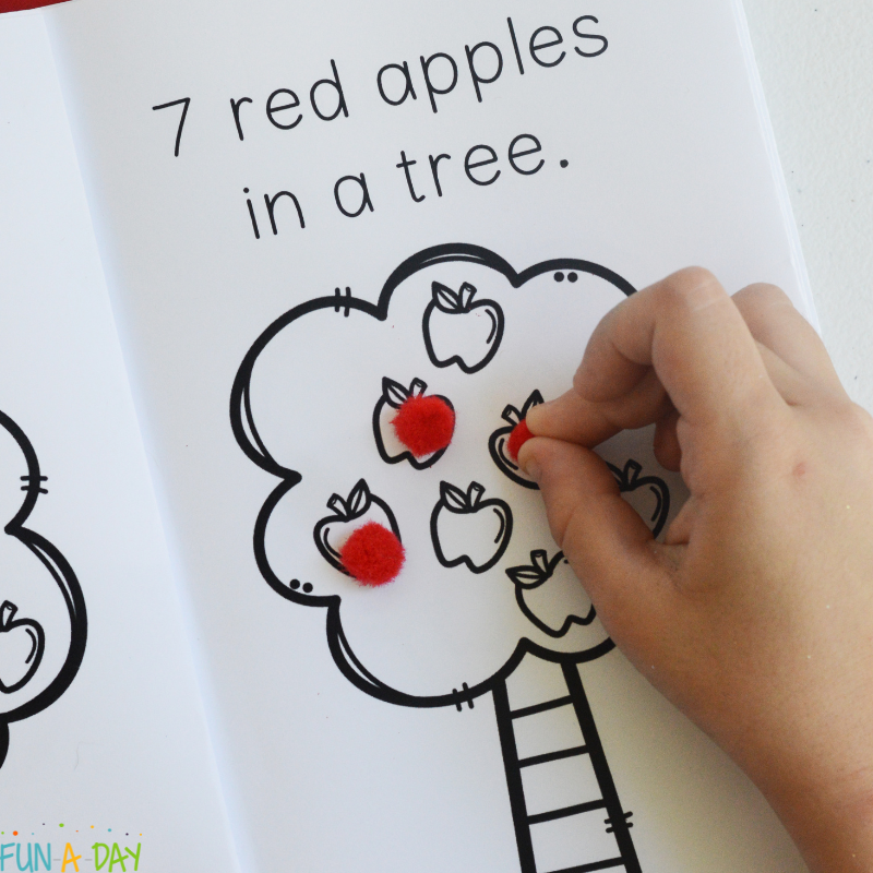Preschooler adding red pom poms to ten red apples mini book
