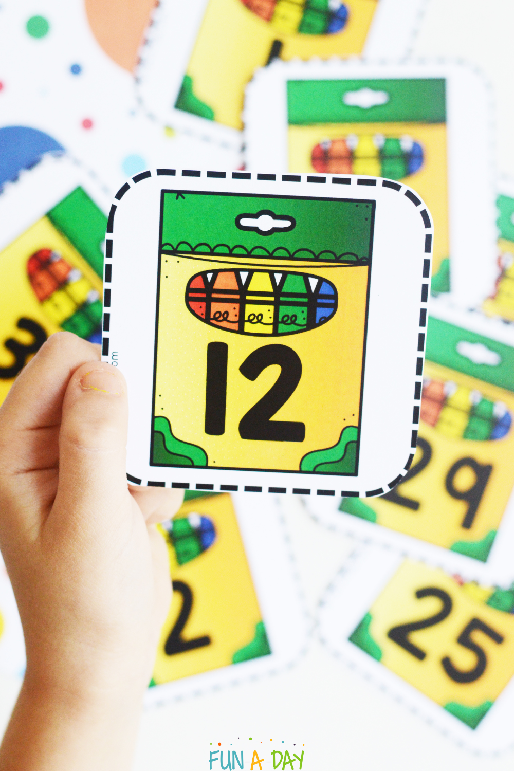 preschool child holding number 12 card over pile of crayon number cards