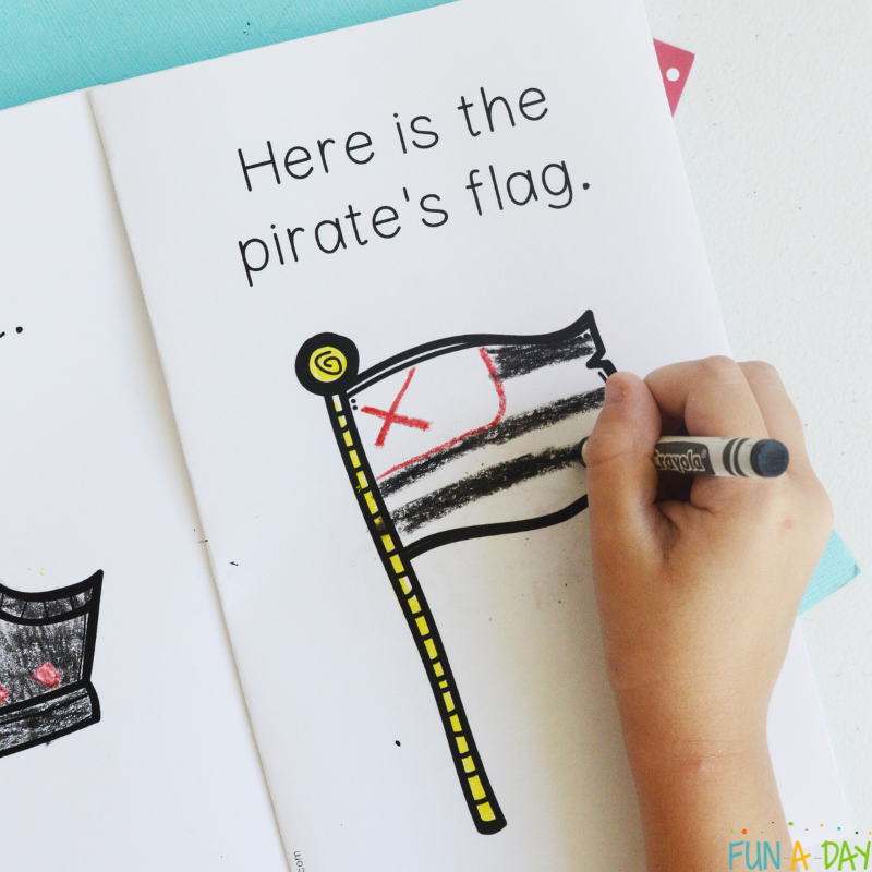 child's hand coloring a pirate flag in a printable emergent reader