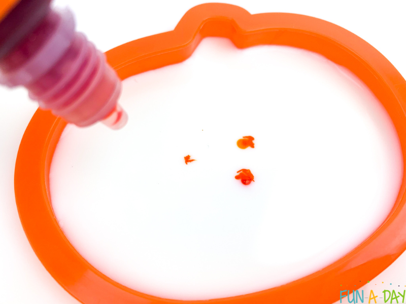 drops of orange food coloring in milk within pumpkin cookie cutter