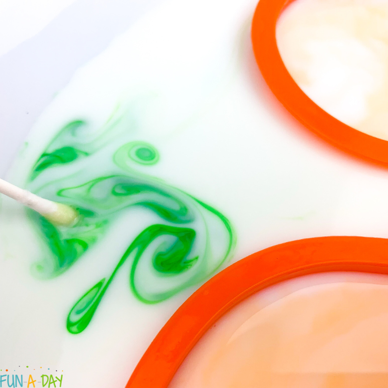 dipping cotton swab in milk with food coloring for magic milk