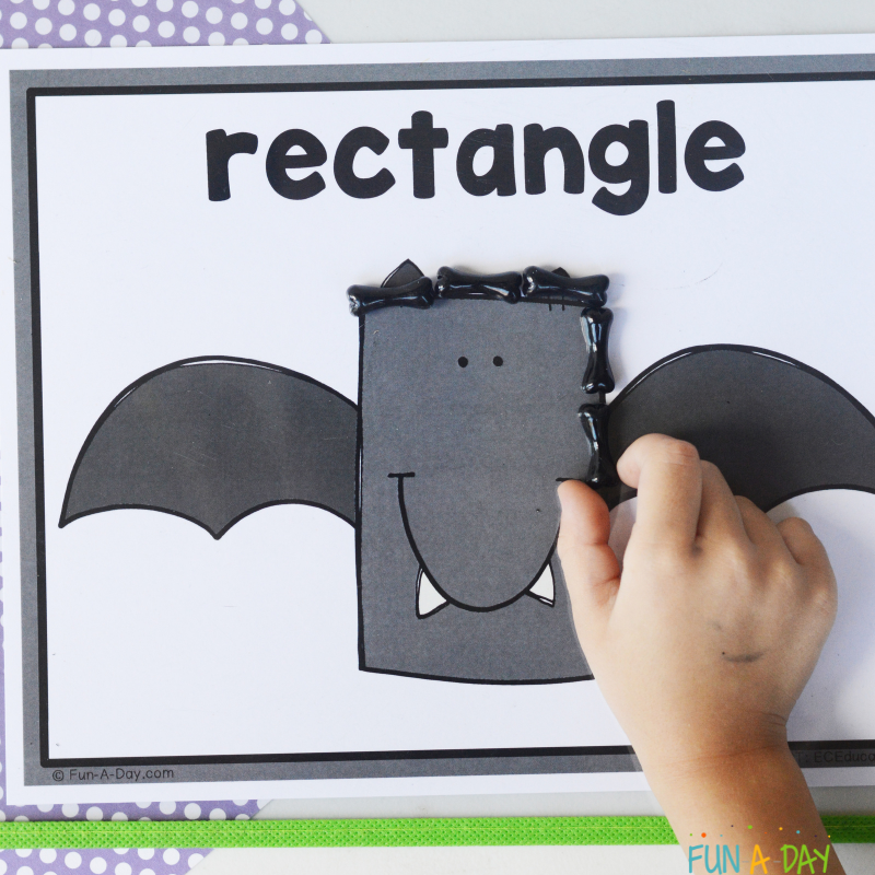 child using black manipulatives to trace around rectangle bat shape mat