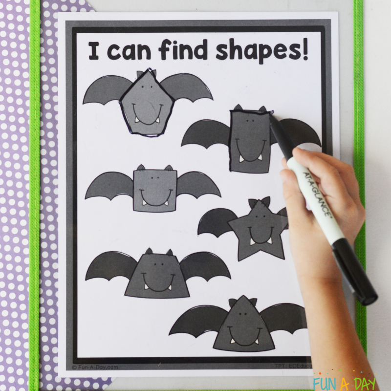 Child using dry erase marker to trace over bat shapes on printable bat shape mats