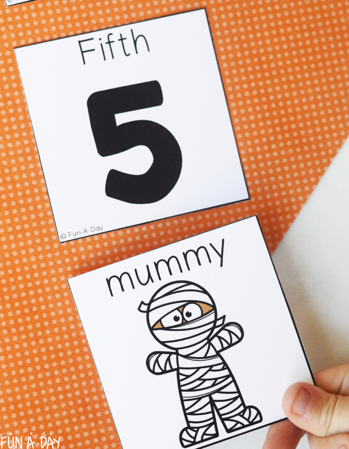 child's hand placing the mummy from Big Pumpkin book underneath the number 5 as part of sequencing activity
