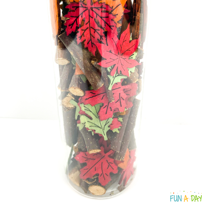 close up of fall sensory bottle with sticks and wooden leaves