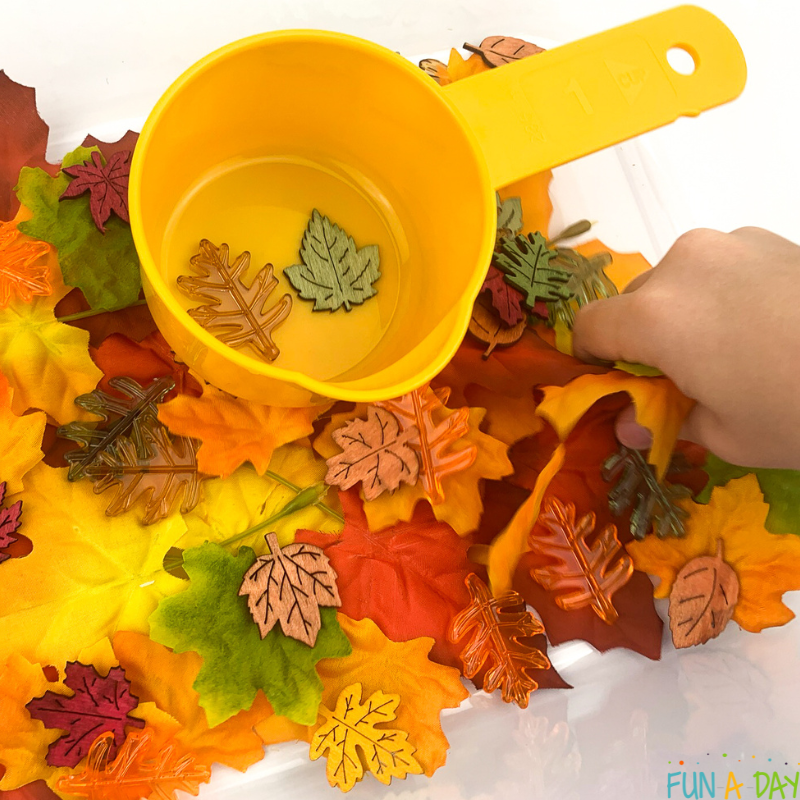 child playing with fake fall leaves in sensory bin