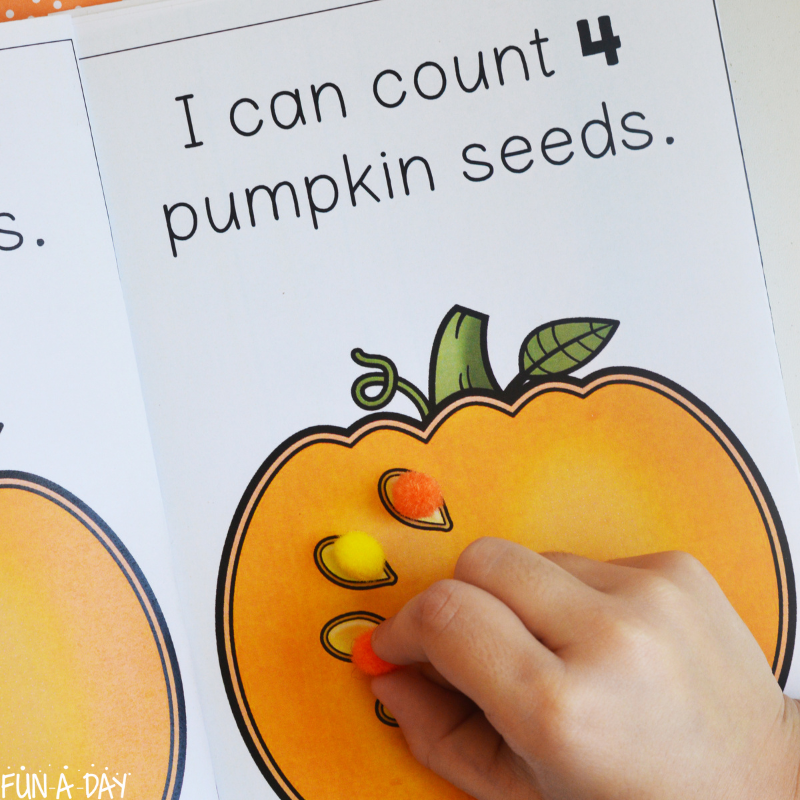 preschool hand placing pompoms on colorful version of pumpkin seed counting book