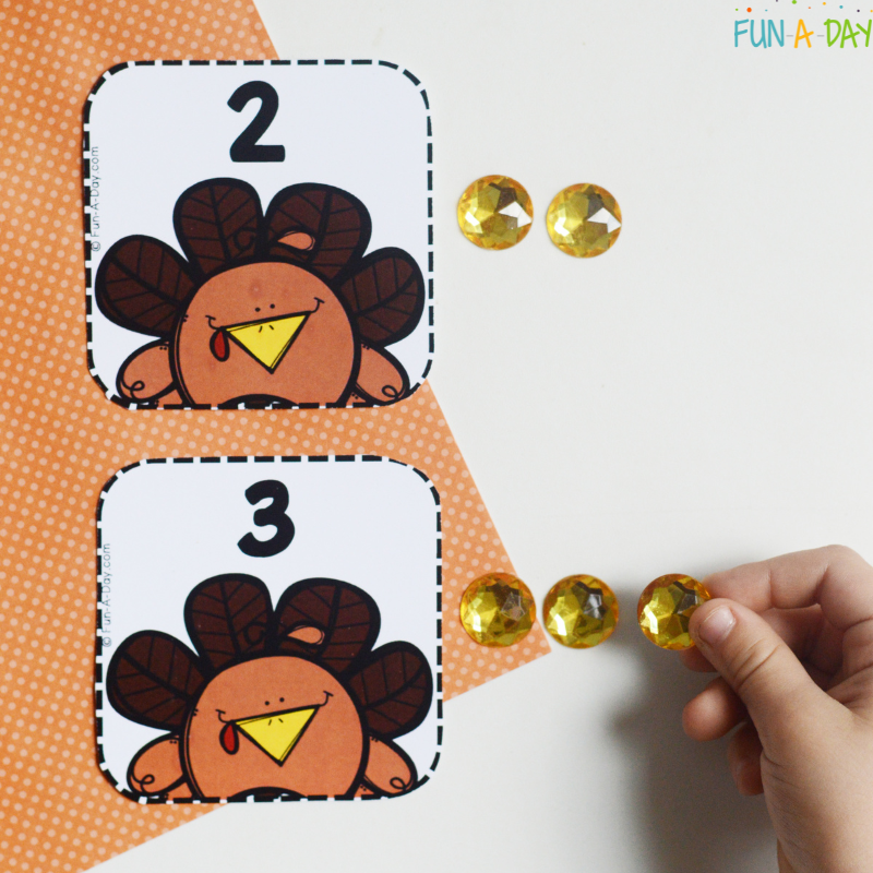 child placing craft gems next to turkey number cards