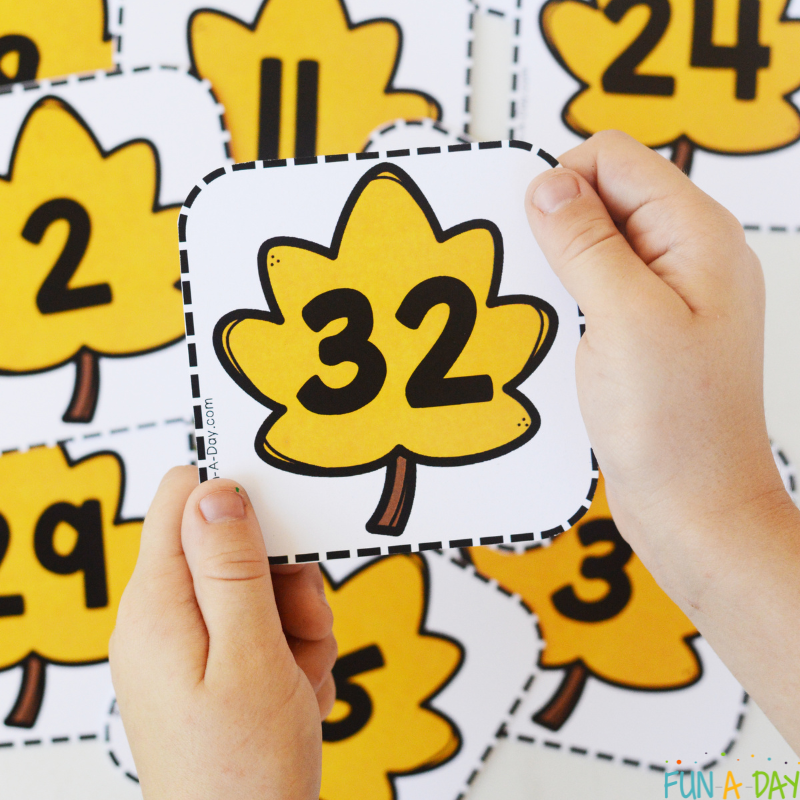child holding leaf number 32 over pile of leaf number cards